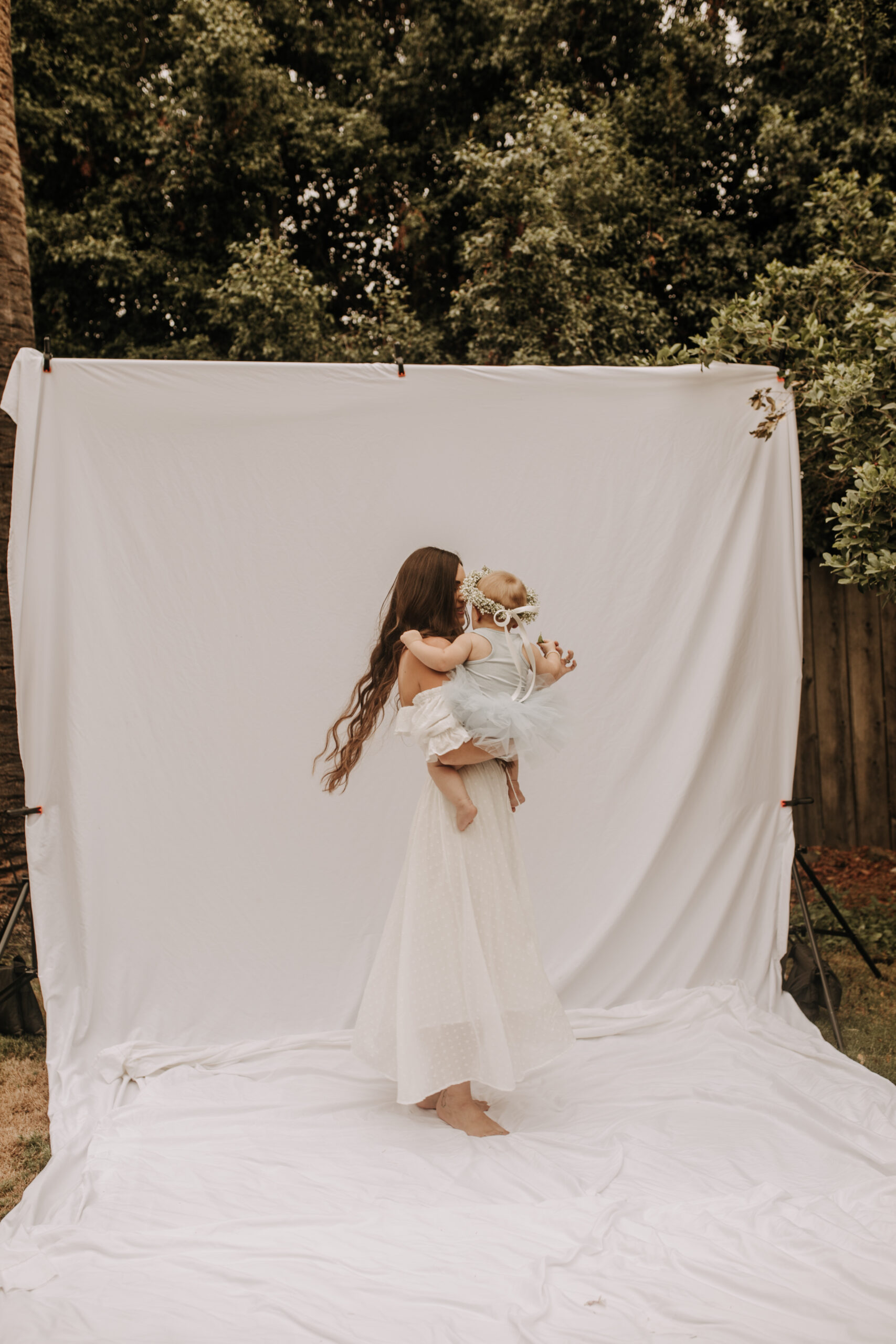 springtime soft light daisies mama and me mom and baby white dress white backdrop flower crown motherhood photos motherhood photography San Diego maternity photographer family photographer Sabrina kinsella outdoor photos green trees backyard mini session