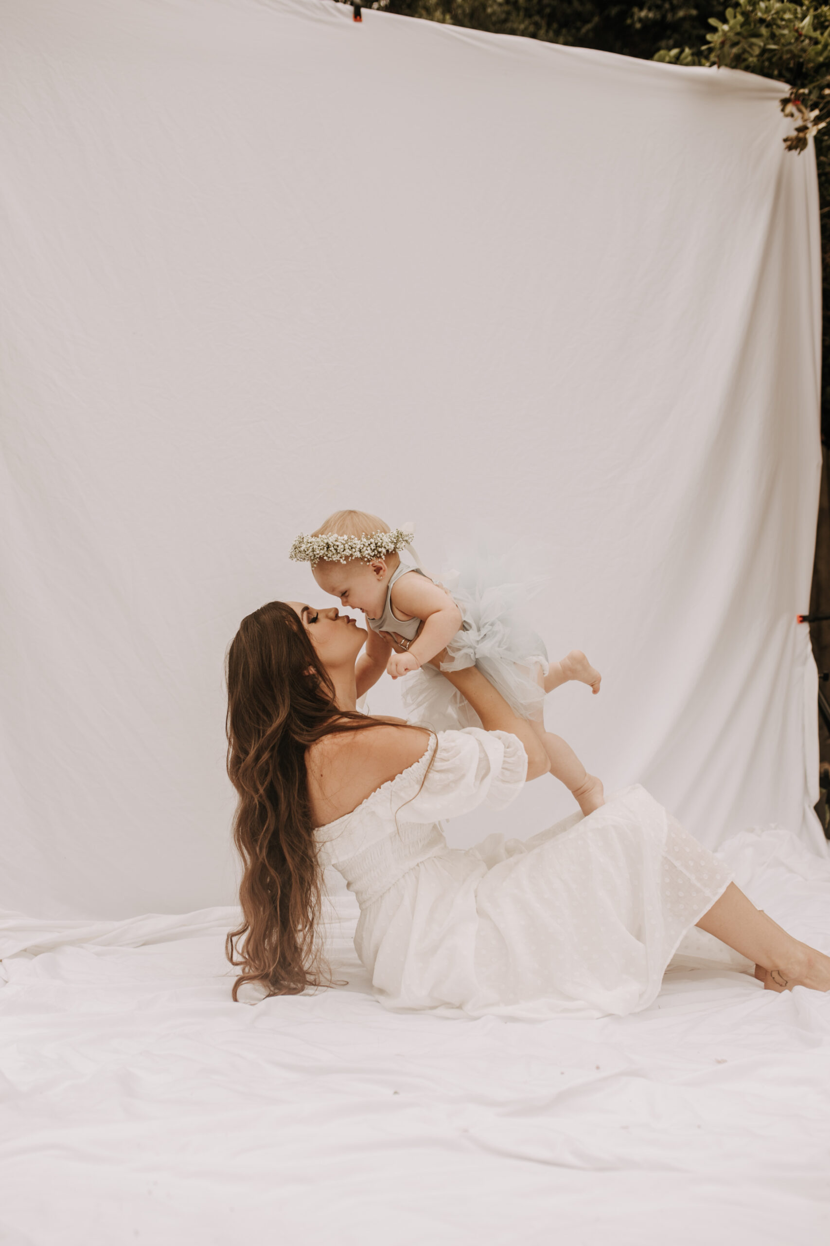 springtime soft light daisies mama and me mom and baby white dress white backdrop flower crown motherhood photos motherhood photography San Diego maternity photographer family photographer Sabrina kinsella outdoor photos green trees backyard mini session