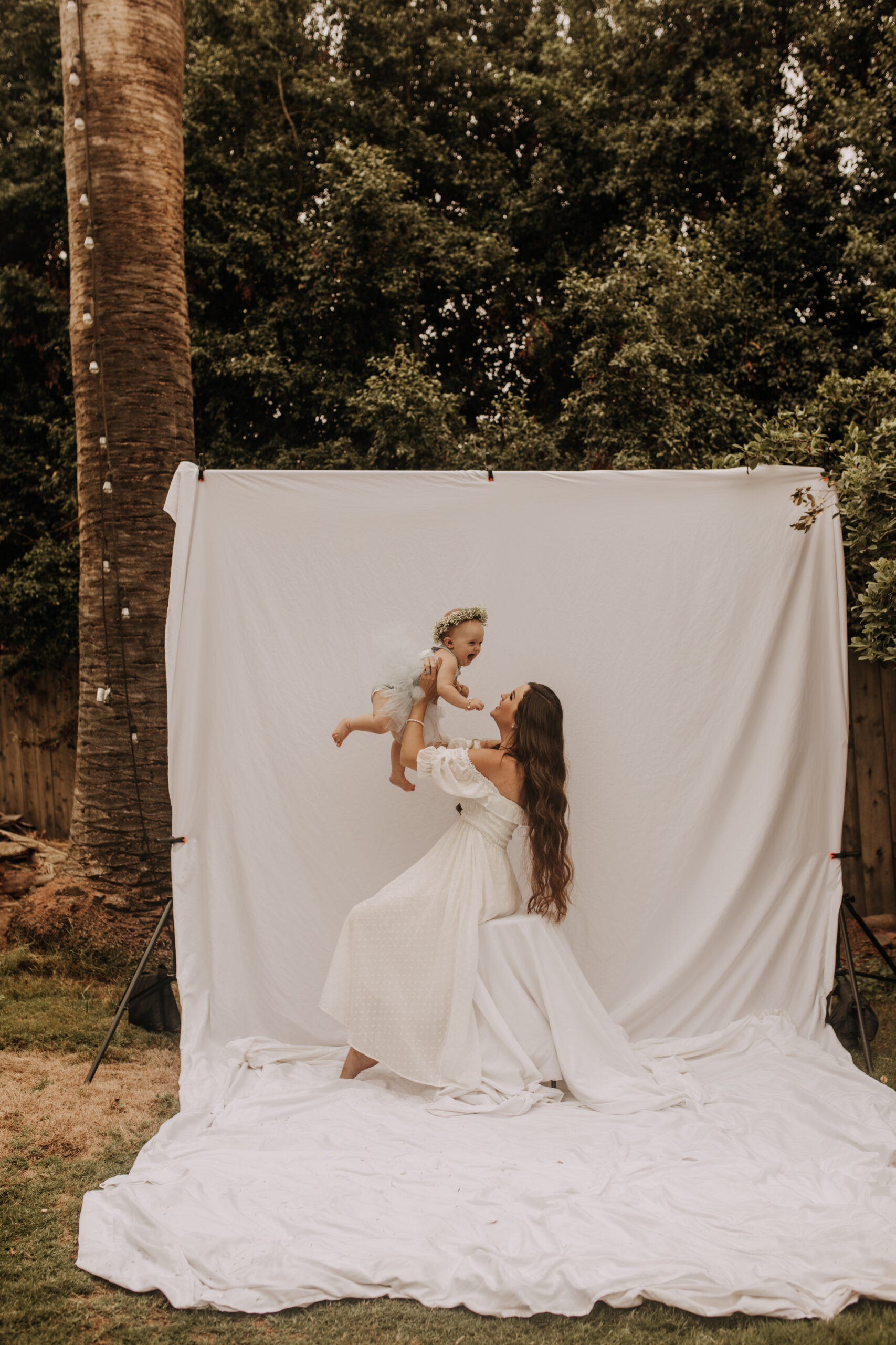 springtime soft light daisies mama and me mom and baby white dress white backdrop flower crown motherhood photos motherhood photography San Diego maternity photographer family photographer Sabrina kinsella outdoor photos green trees backyard mini session