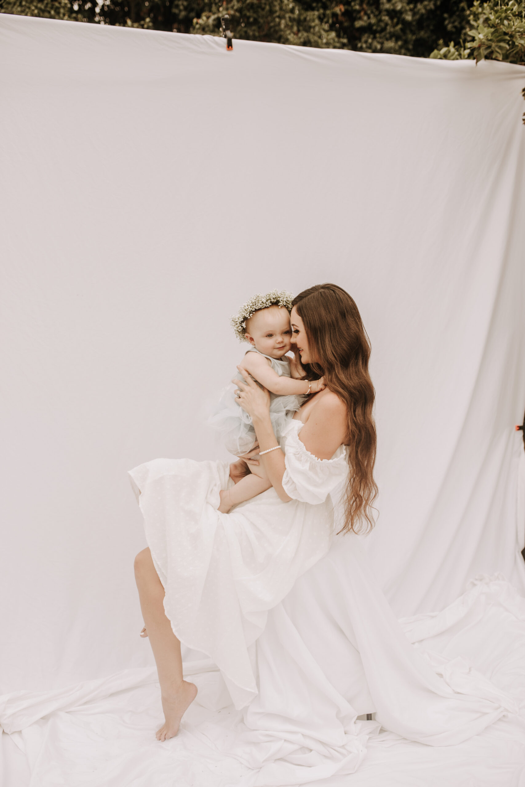 springtime soft light daisies mama and me mom and baby white dress white backdrop flower crown motherhood photos motherhood photography San Diego maternity photographer family photographer Sabrina kinsella outdoor photos green trees backyard mini session